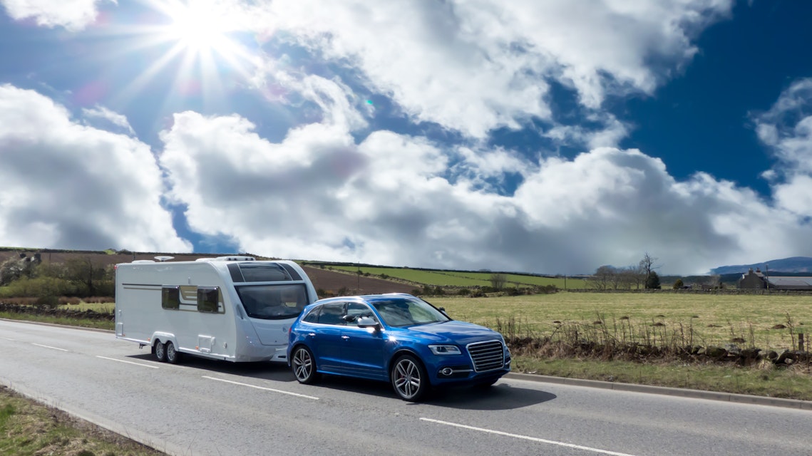 Blue car travelling on road with caravan.