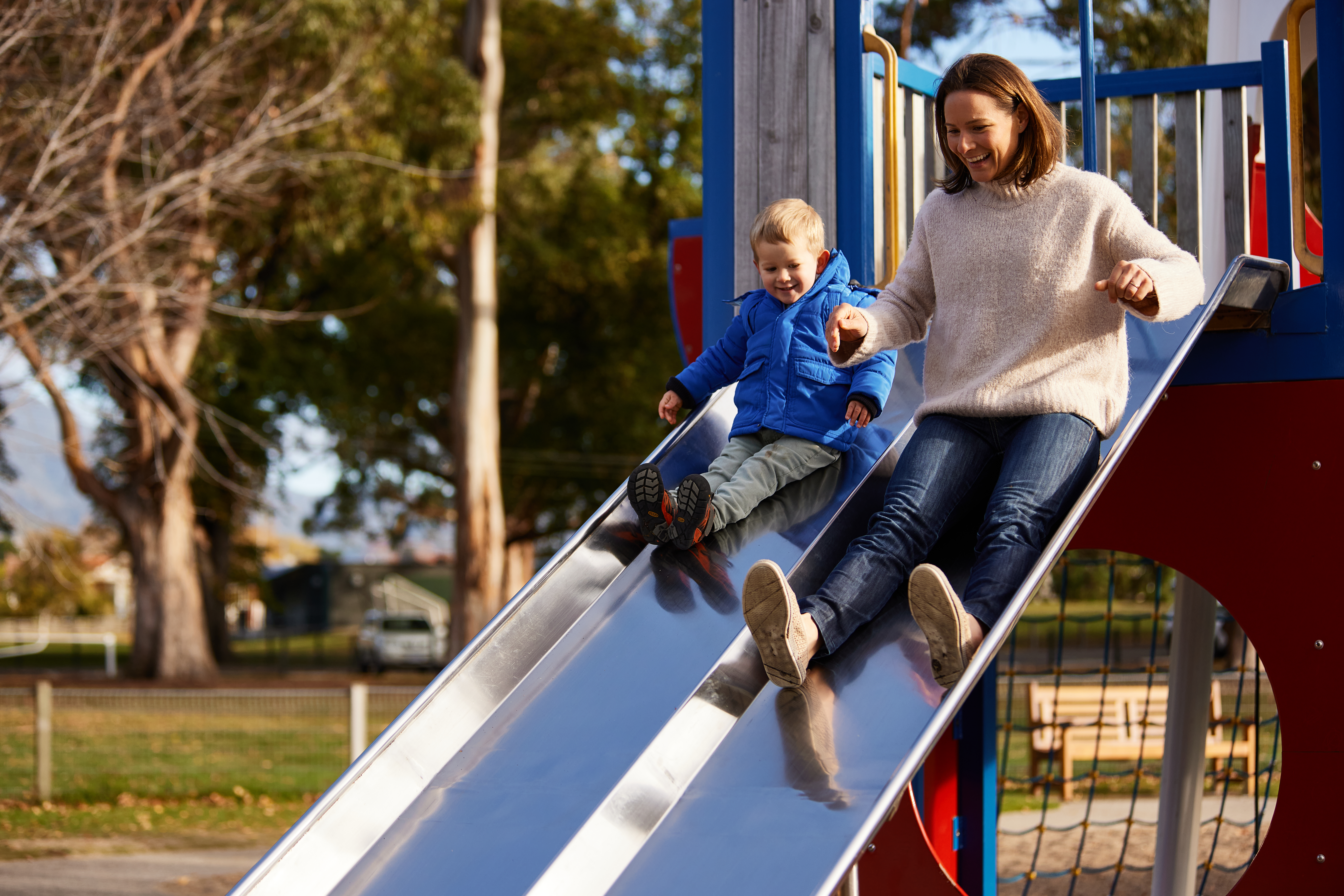 Mum and son sliding down slide at park.
