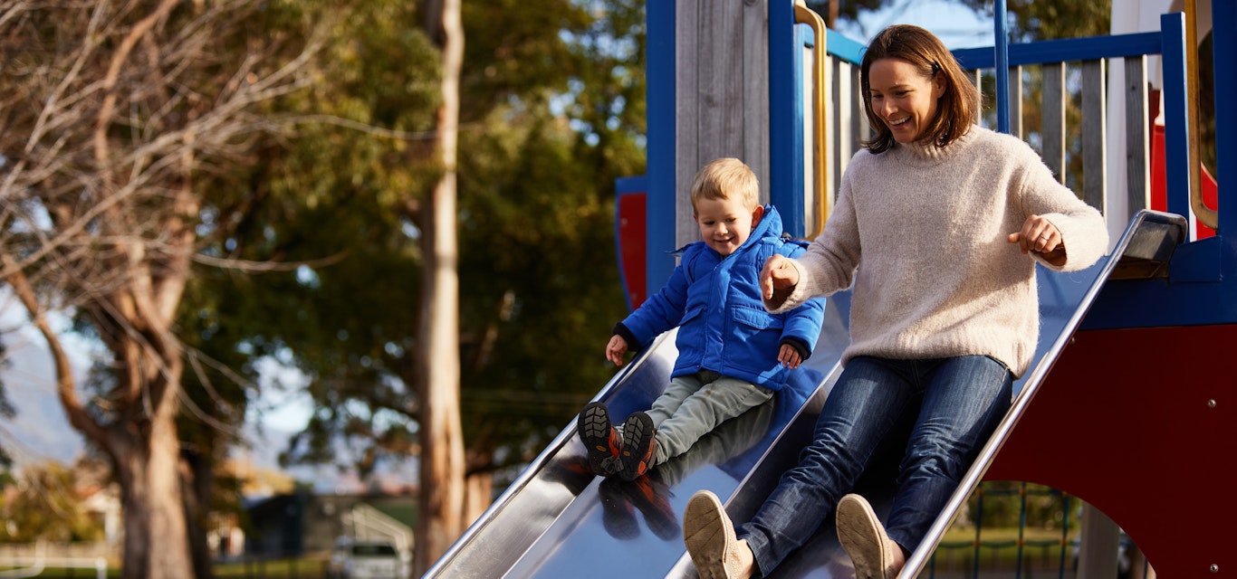 Mum and son sliding down slide at park.