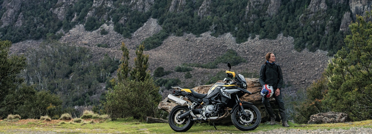 woman leaning against rock with motorbike in foreground