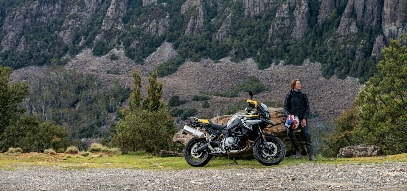 Taking a scenic break woman leaning against rock with motorbike in foreground