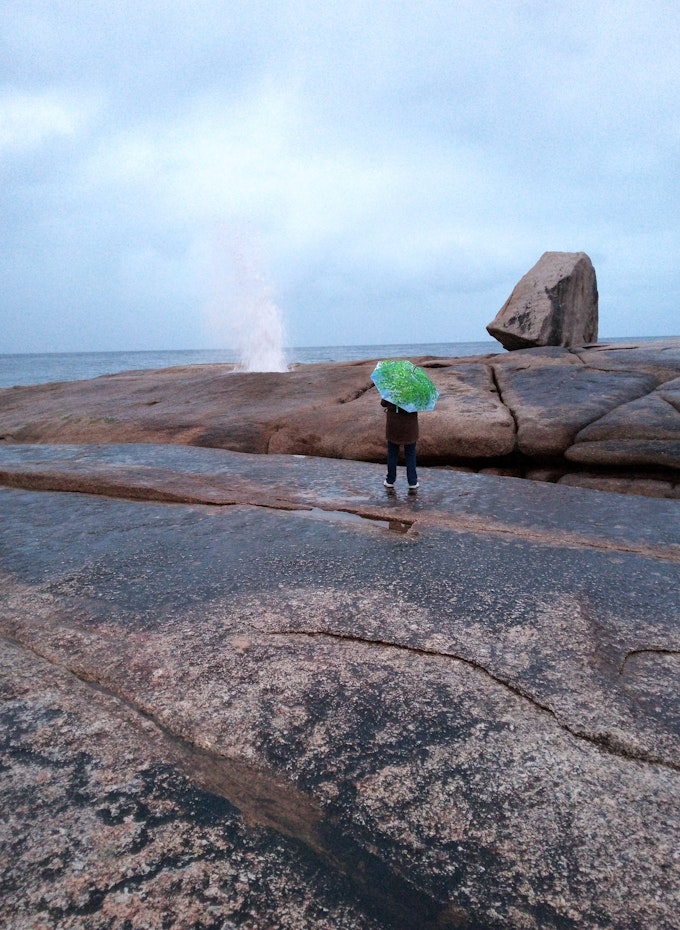 woman with umbrella standing near blowhole 