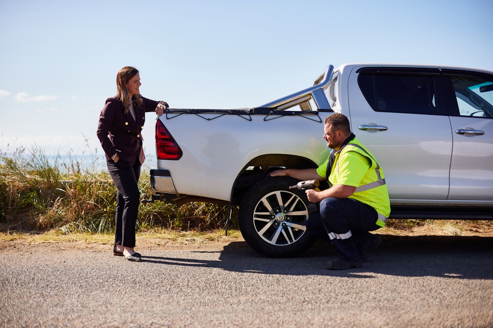Business woman watching on as roadside patrol changes tyre on her car