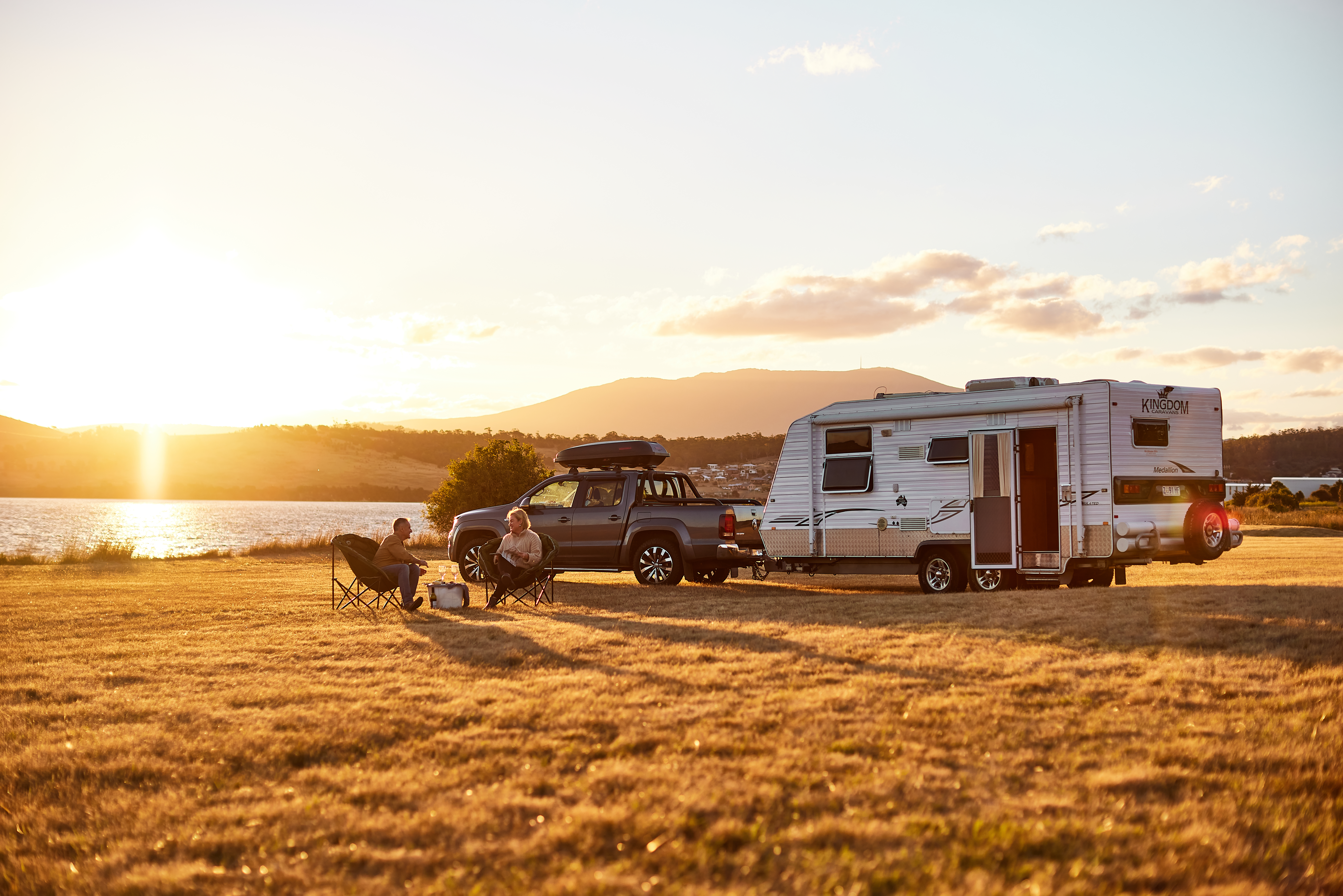 Couple relaxing outside caravan at sunset.