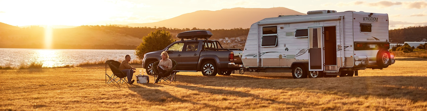 Couple relaxing outside caravan at sunset.