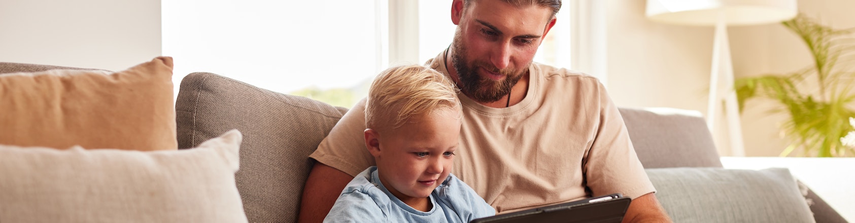 Dad and son sitting on couch looking at tablet.
