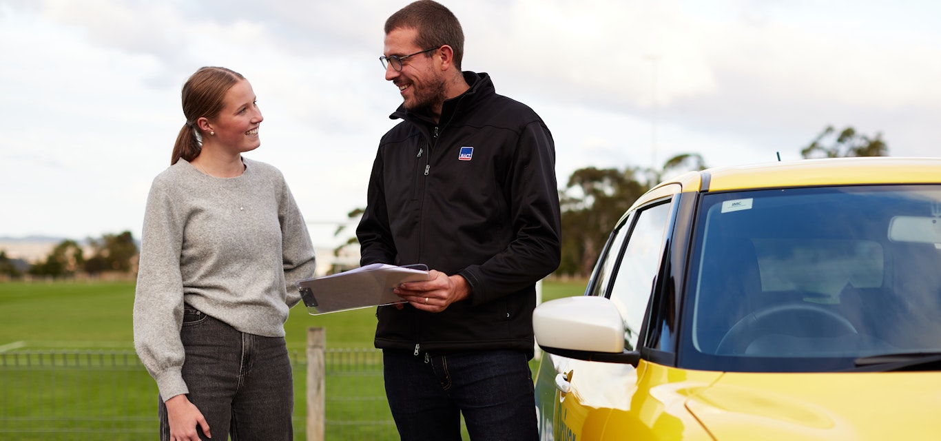 Learner driver and instructor standing near car