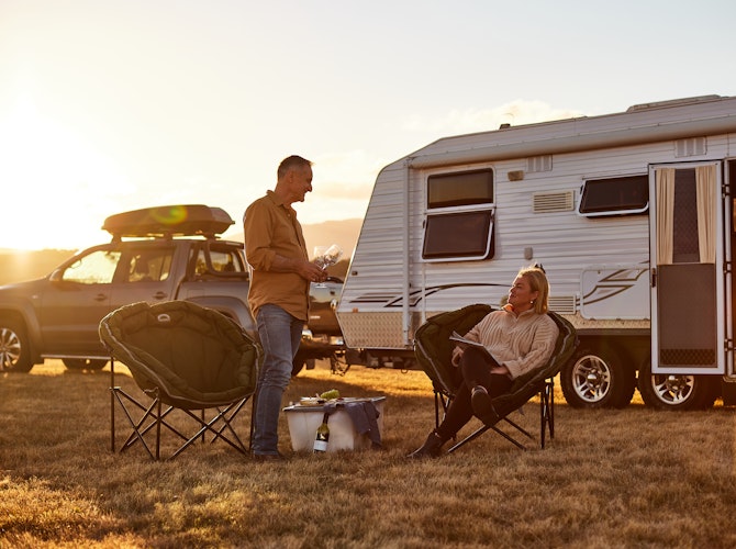 Couple having dinner in front of their caravan with the sun setting.