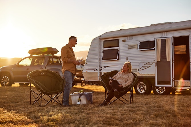 Couple having dinner in front of their caravan with the sun setting.