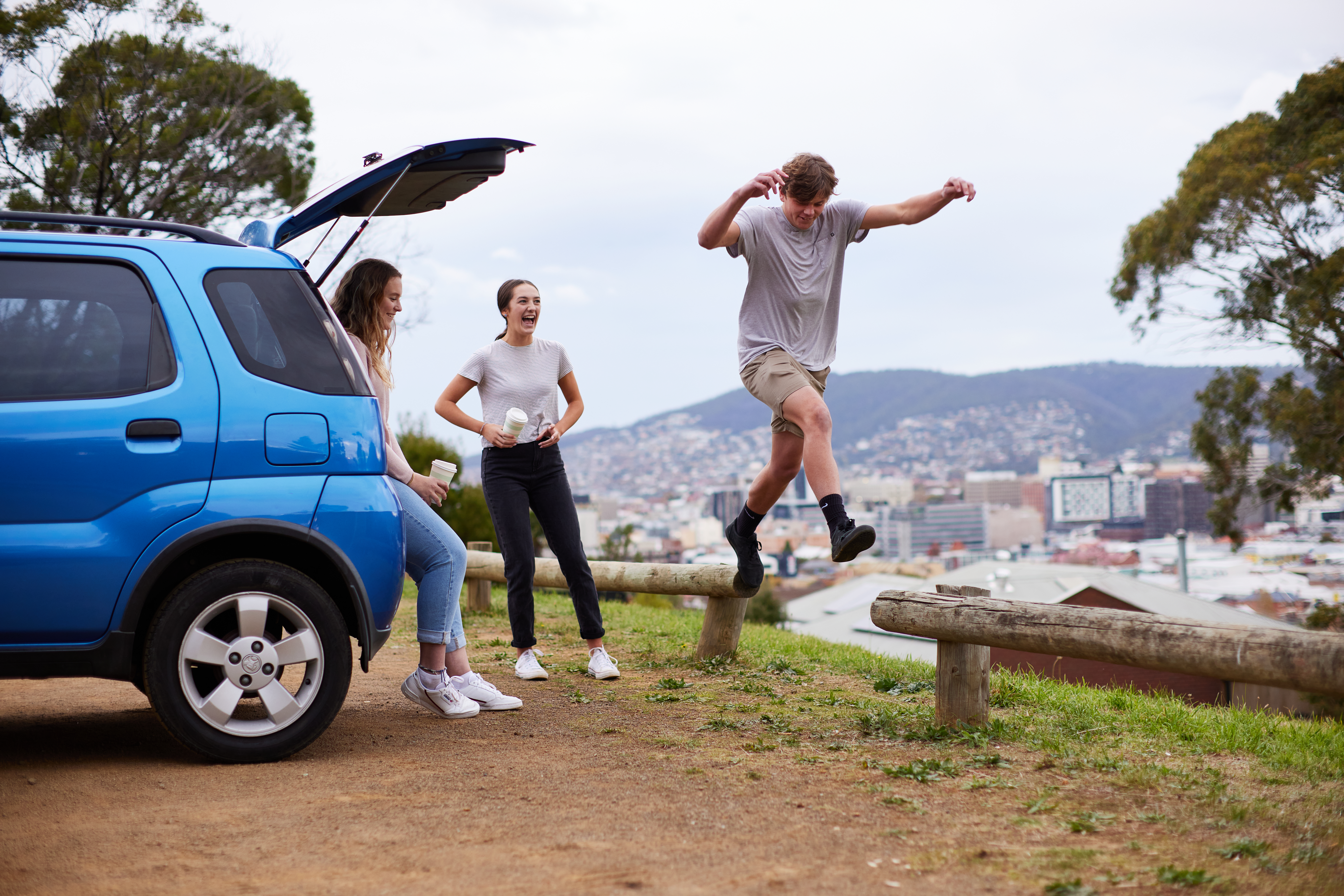 Youths jumping around car in park.