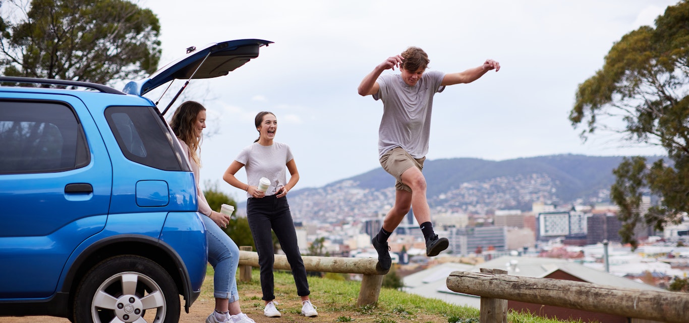 Youths jumping around car in park.