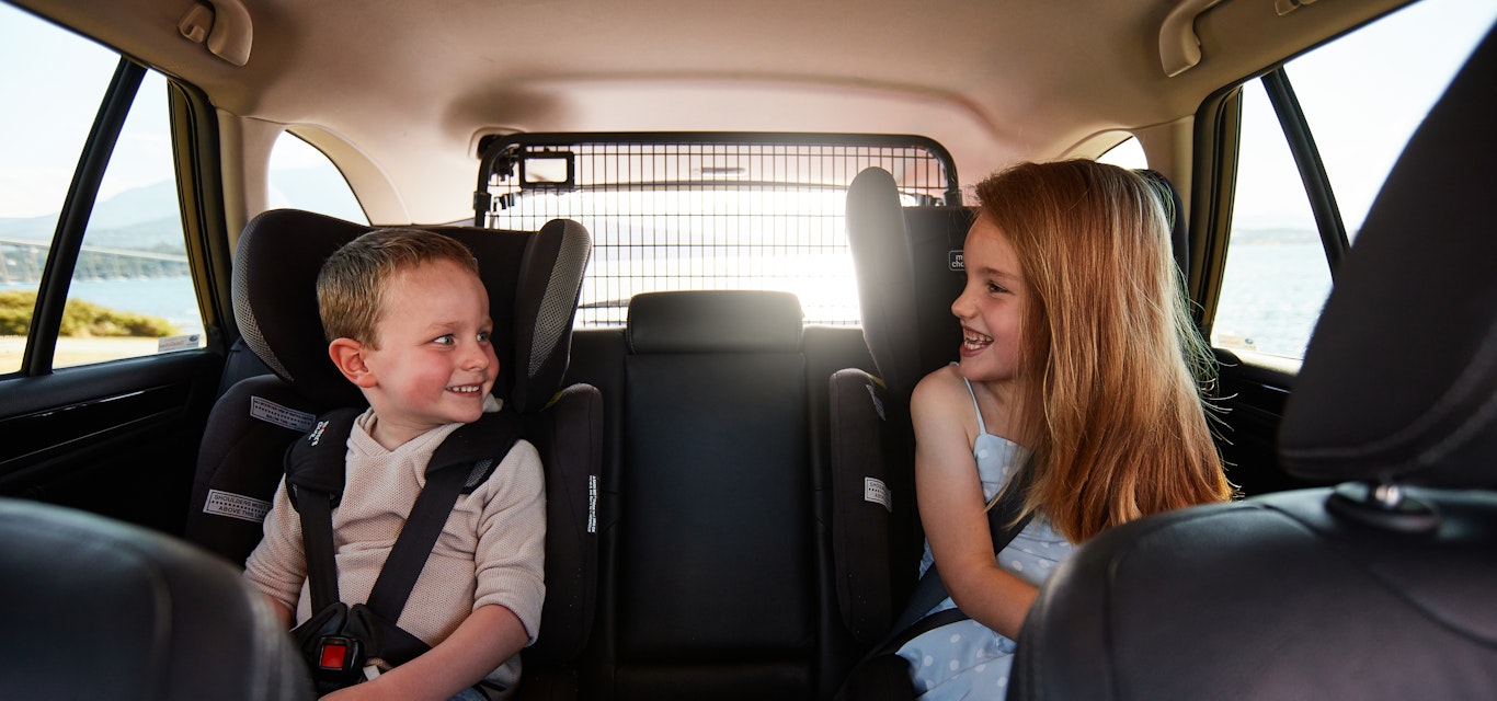Two kids looking at each other, in car seats