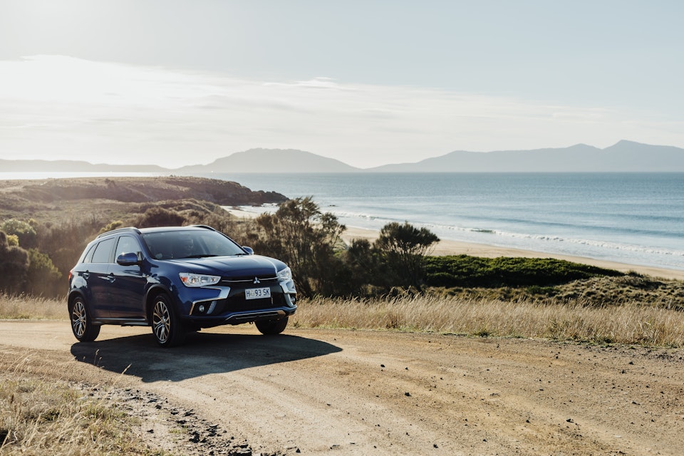 car on gravel road with water in background