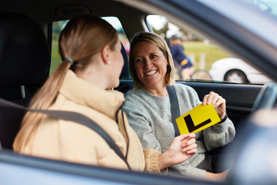 Mother and daughter holding learner plate in vehicle