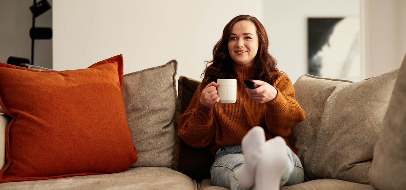 Lady sitting on couch changing tv channels.