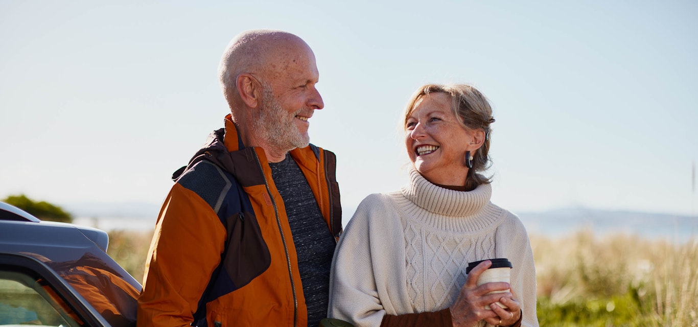 Senior couple standing next to car with coffee