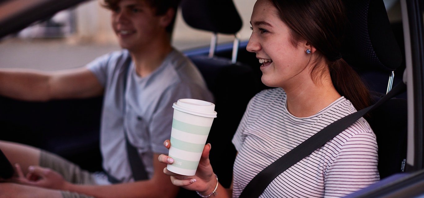 Young adults driving a car with coffee