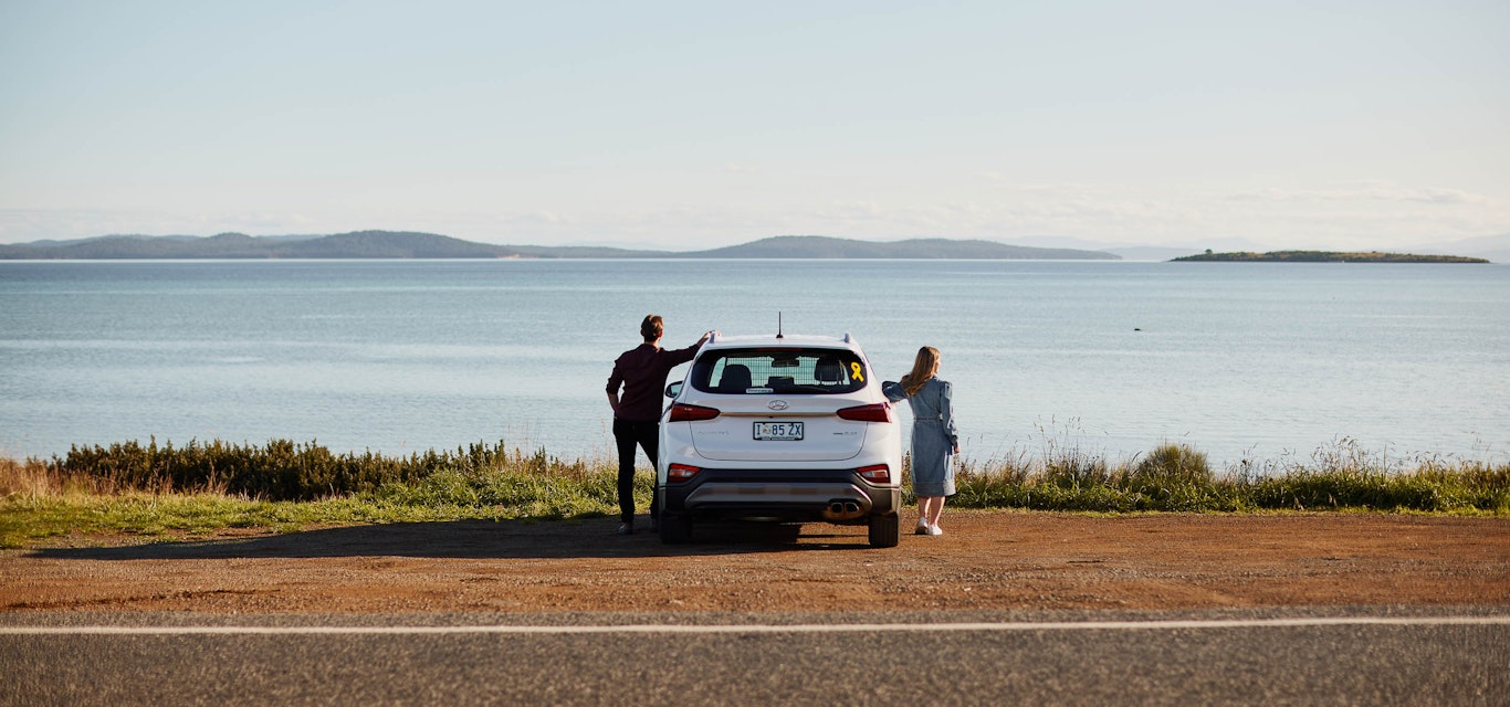 Couple standing beside their car parked behind the ocean
