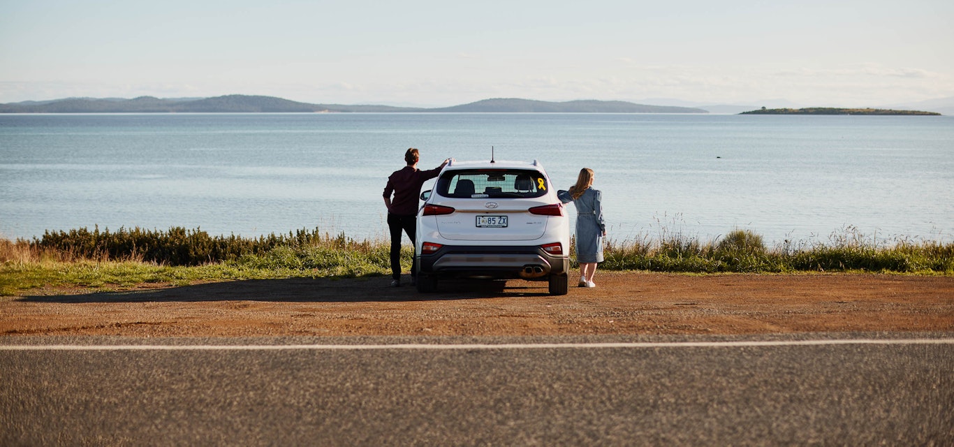 Couple standing beside their car parked behind the ocean