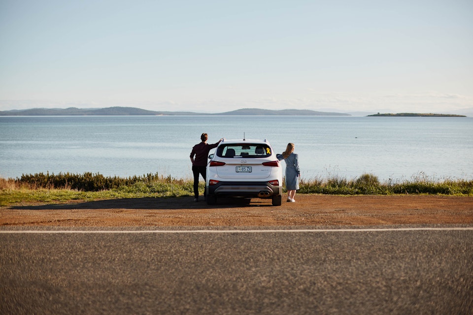 Couple standing beside their car parked behind the ocean