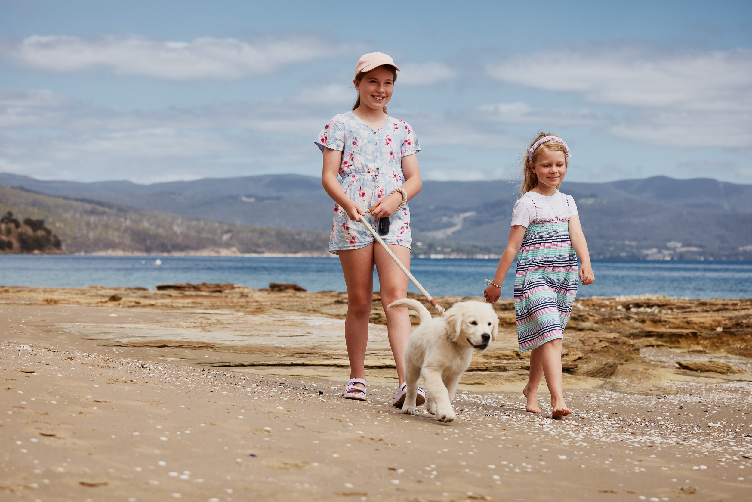 Young girls walking golden retriever puppy on beach