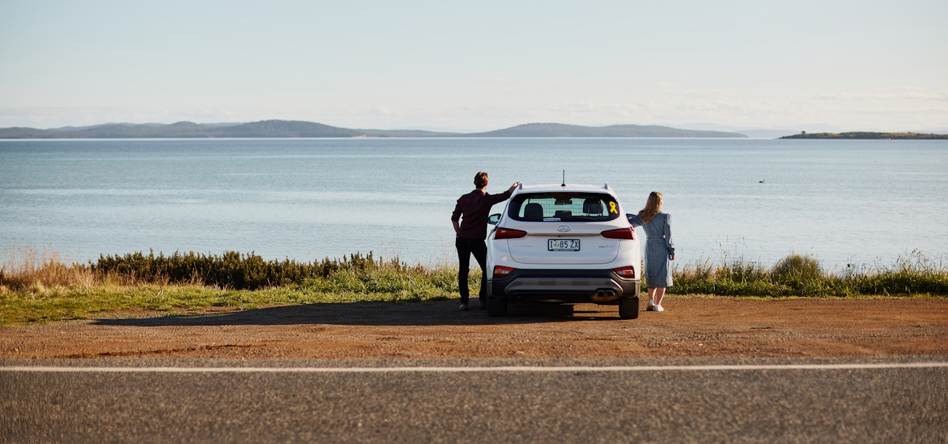 Man and woman standing next to a car and looking into the distance