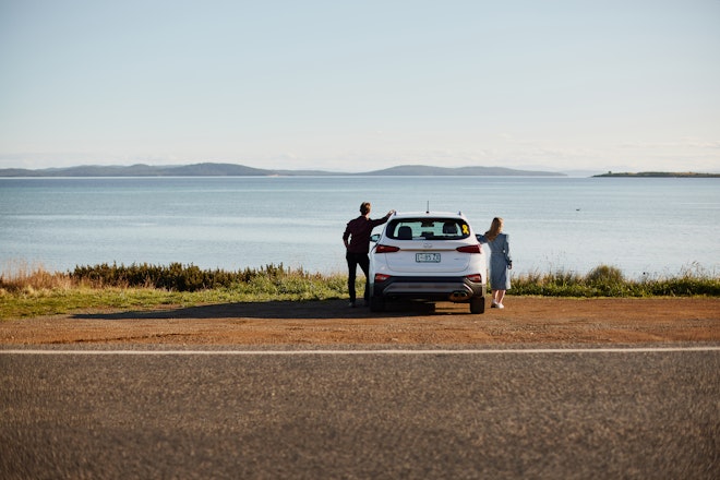 Man and woman standing next to a car and looking into the distance