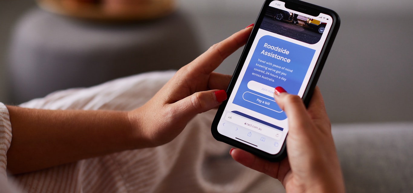Roadside members will receive renewals directly to their email on file. A woman's hands hold a mobile phone with a screen on the RACT Roadside page.