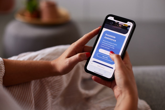 A woman's hands hold a mobile phone with a screen on the RACT Roadside page.