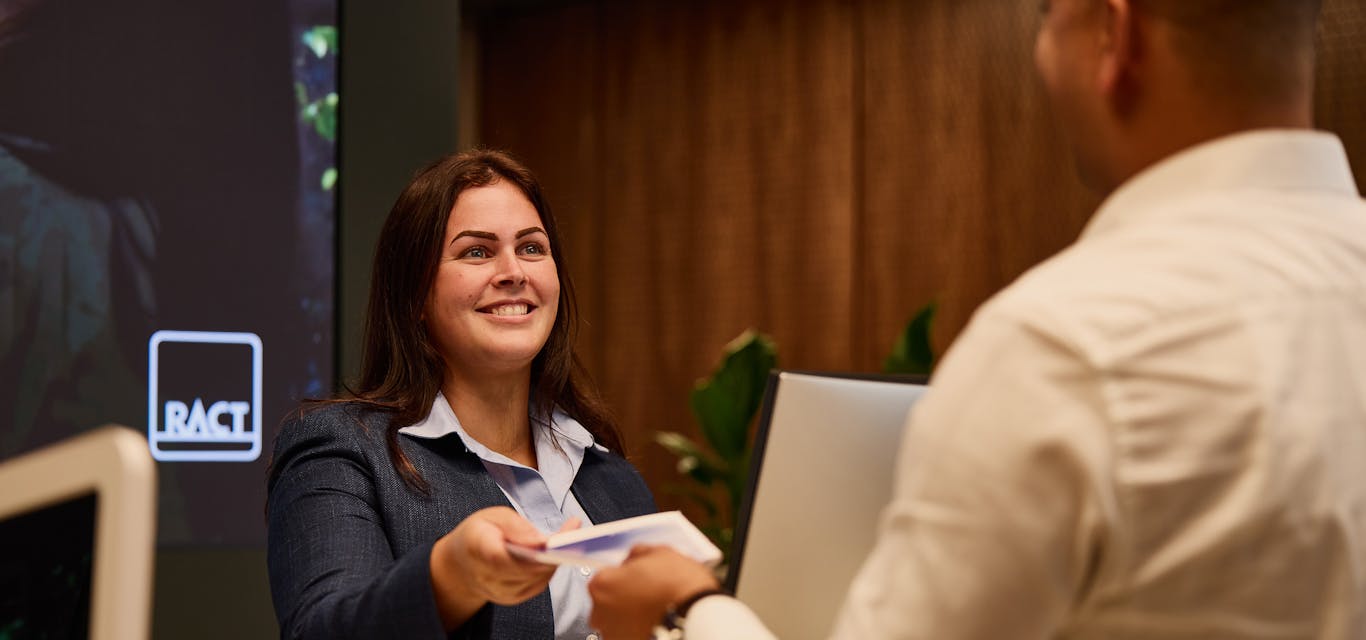 The new Kingston store has been designed with our members in mind. A female concierge hands a male customer paperwork at an RACT counter.