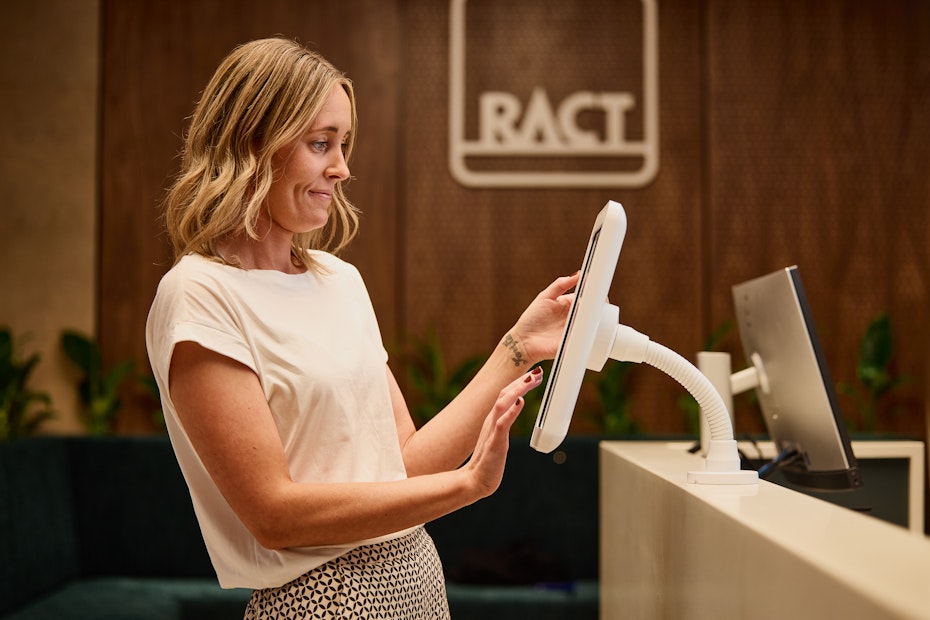 A blonde woman in a white shirt uses a touchscreen computer.