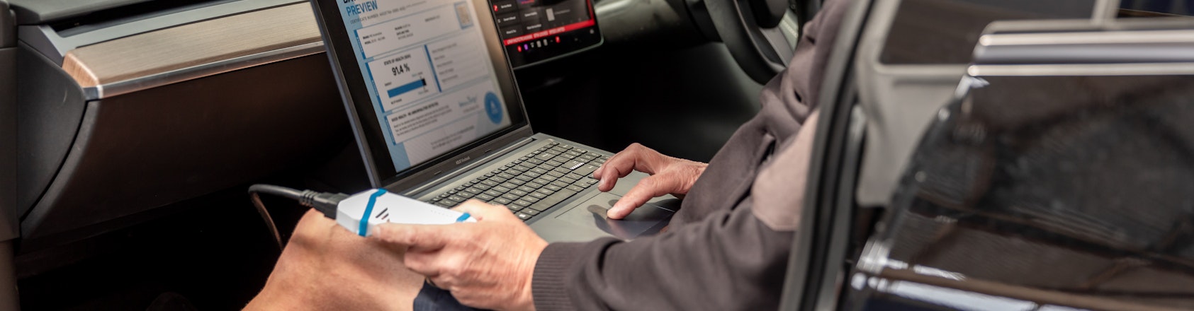 The EV battery testing process is quick, efficient and effective. A man holds a battery testing unit and laptop while seated in the passenger seat of an electric vehicle.