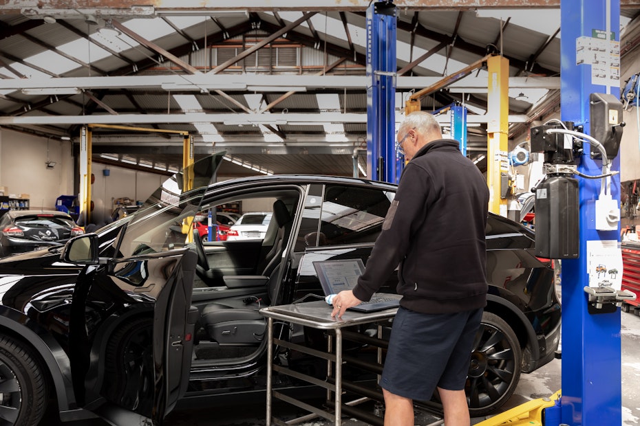 A man stands at a rolling table next to a car, with a laptop open.