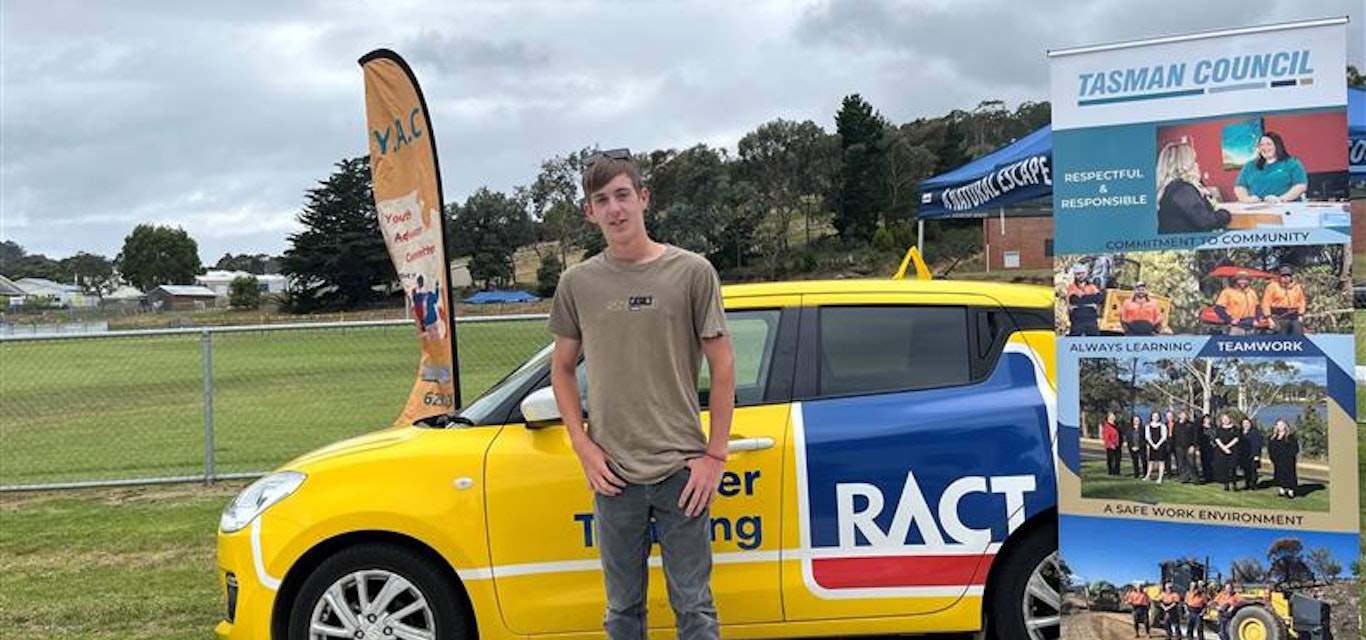 A young man stands in front of a Driver Training car.