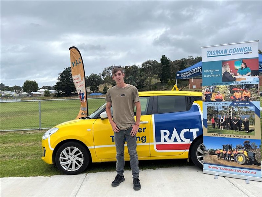 A young man stands in front of a Driver Training car.