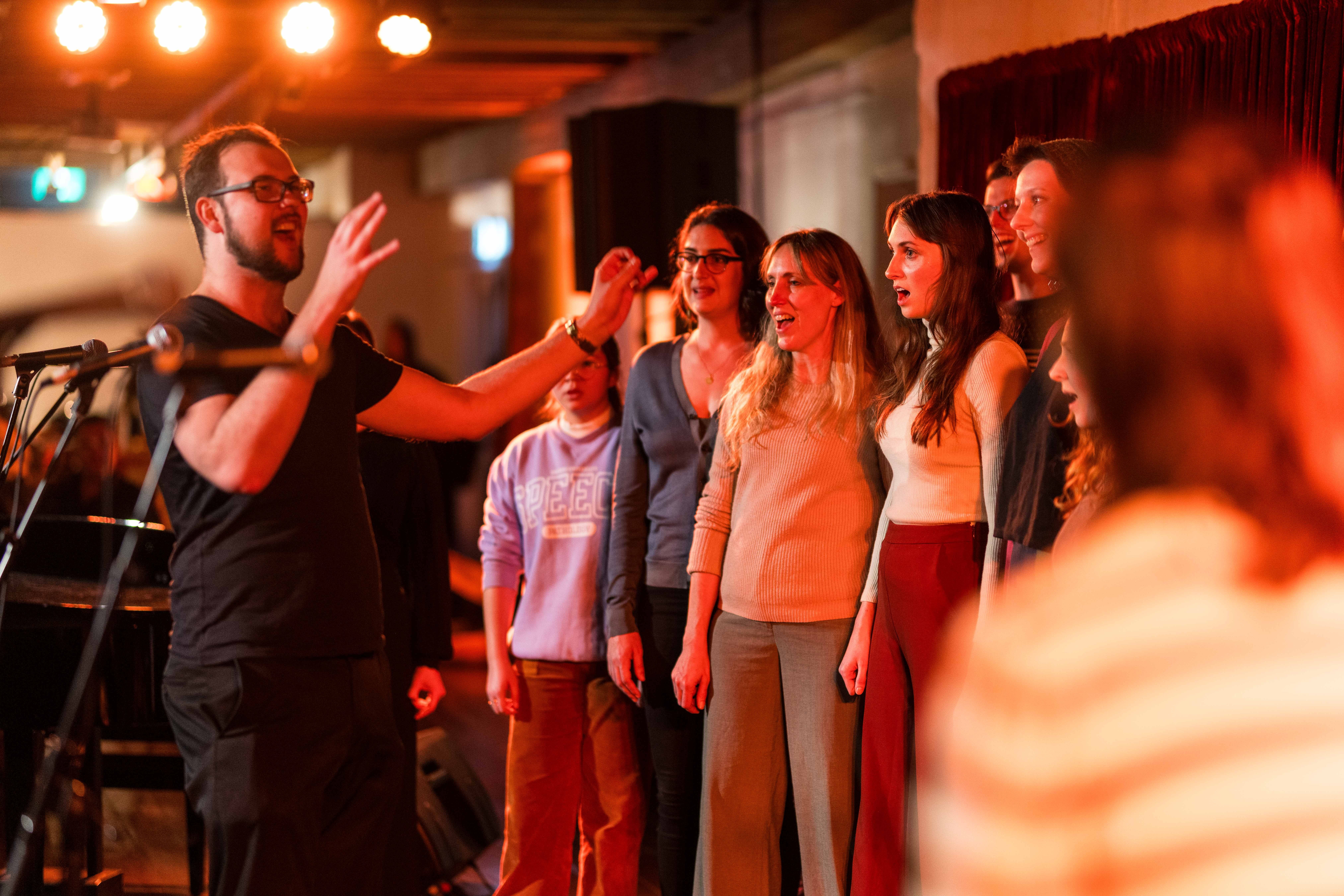 A smiling man leads a group of people in song