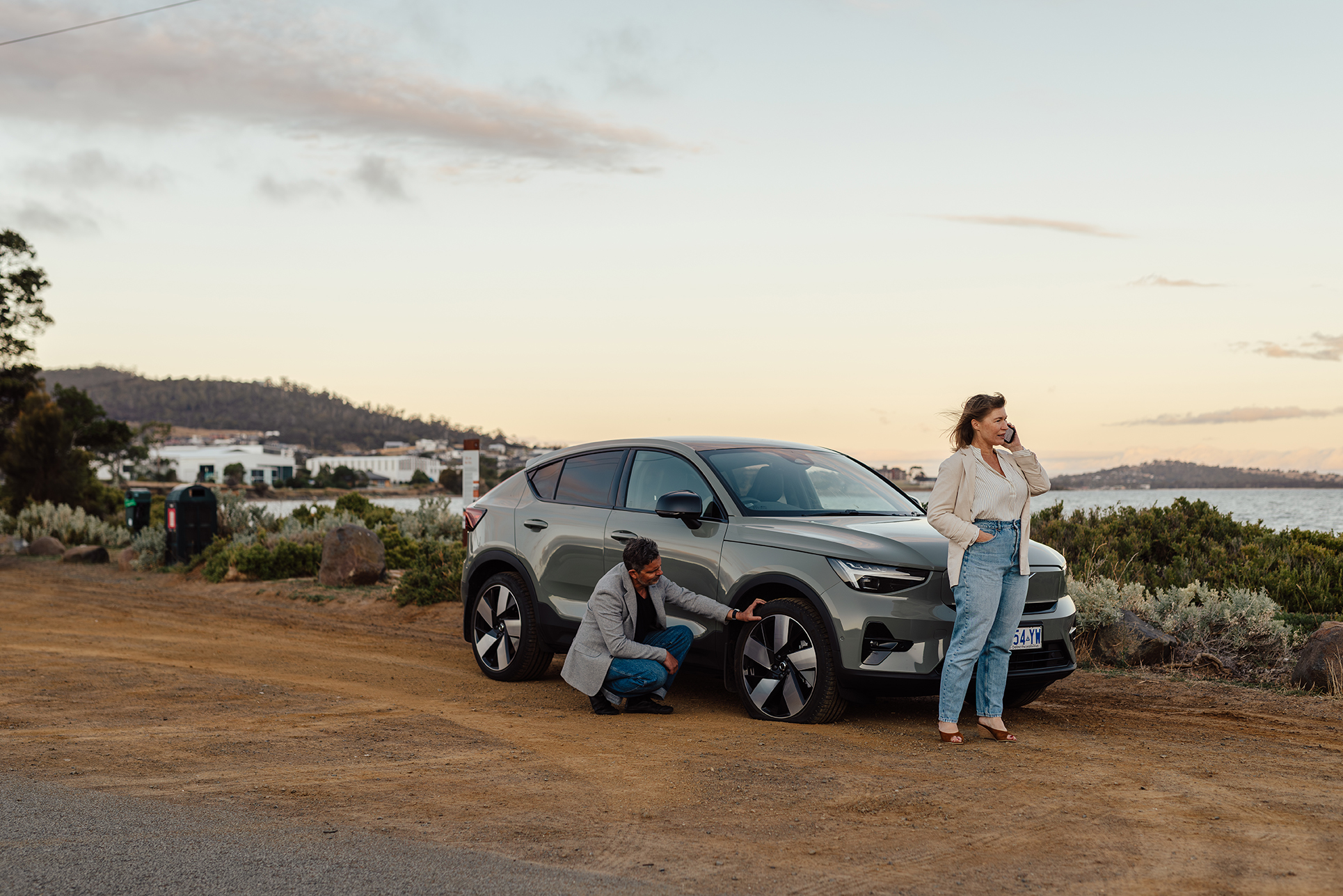 Man and woman standing next to their broken down car, woman is on the phone
