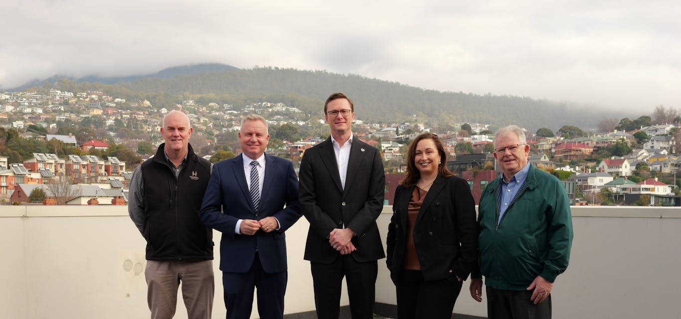 Steve Old (Tasmanian Hospitality Association), Premier Jeremy Rockliff, Mark Mugnioni (RACT), Amy Hills (TICT) and Robert Mallett (Small Industry Council of Tasmania) Four men and a woman stand on a corporate deck with suburbs and a mountain behind on an overcast day