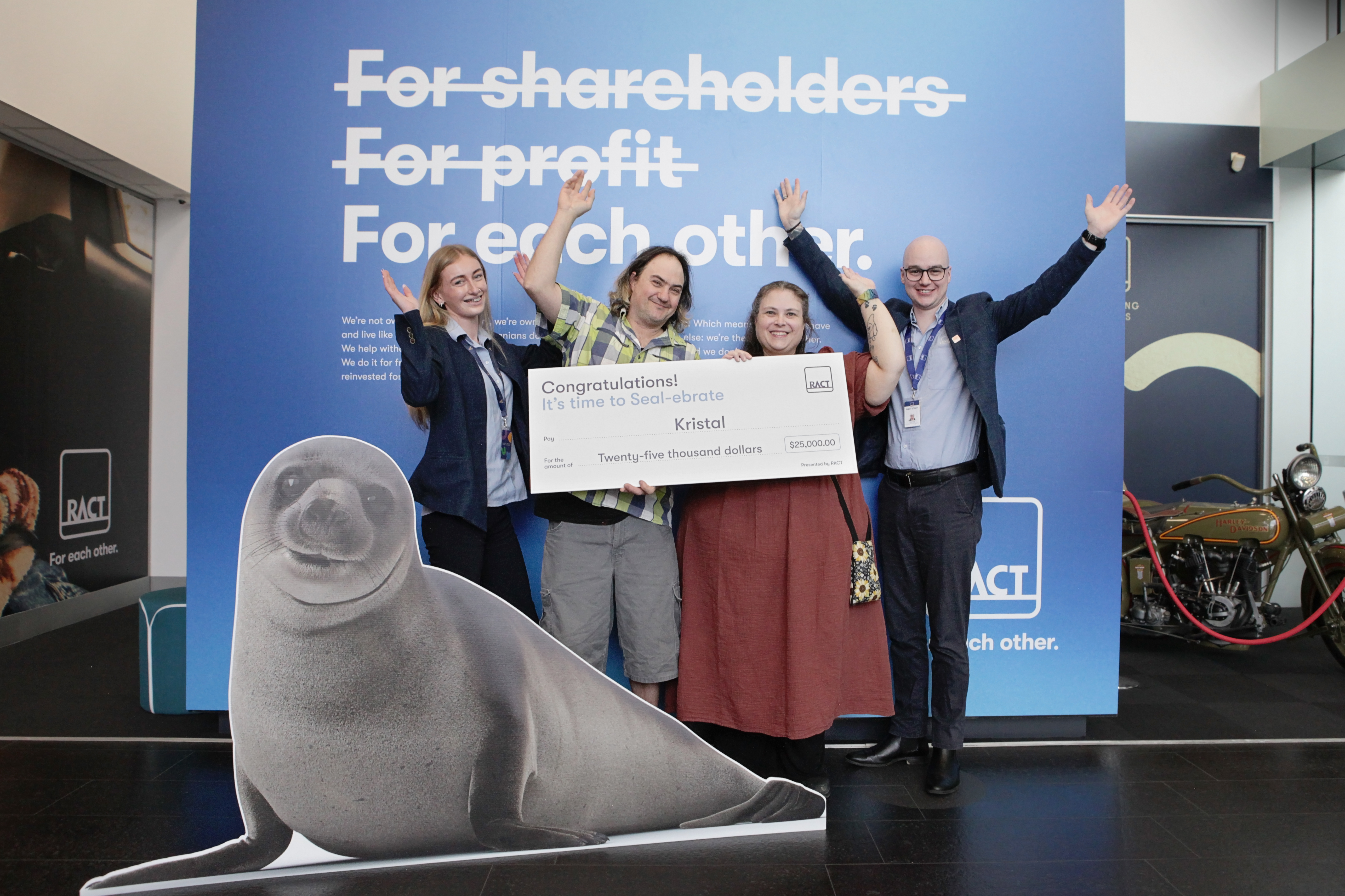 Four people smile with their hands up with a novelty cheque