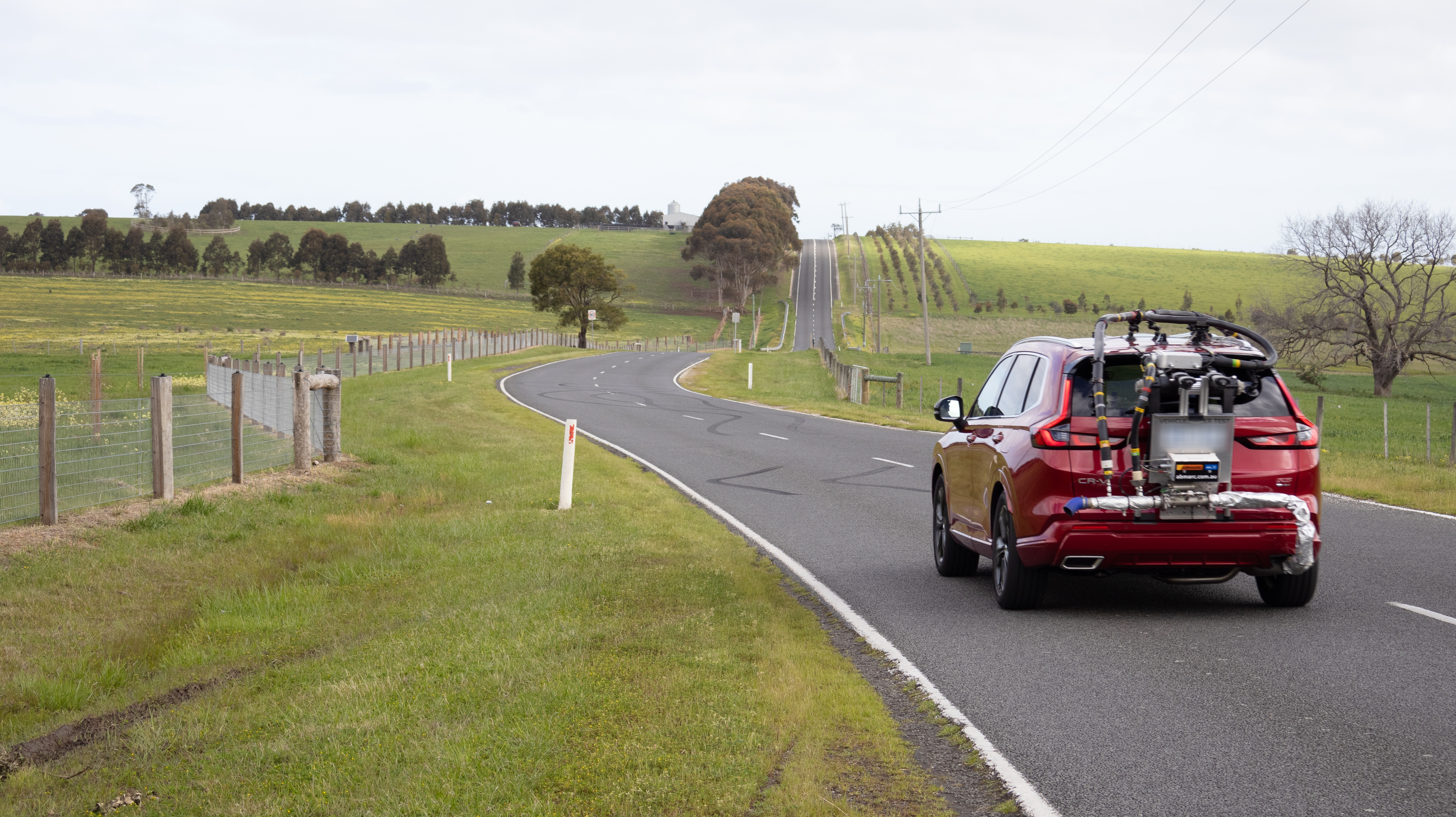 A red car with a testing contraption drives on a rural Victorianroad