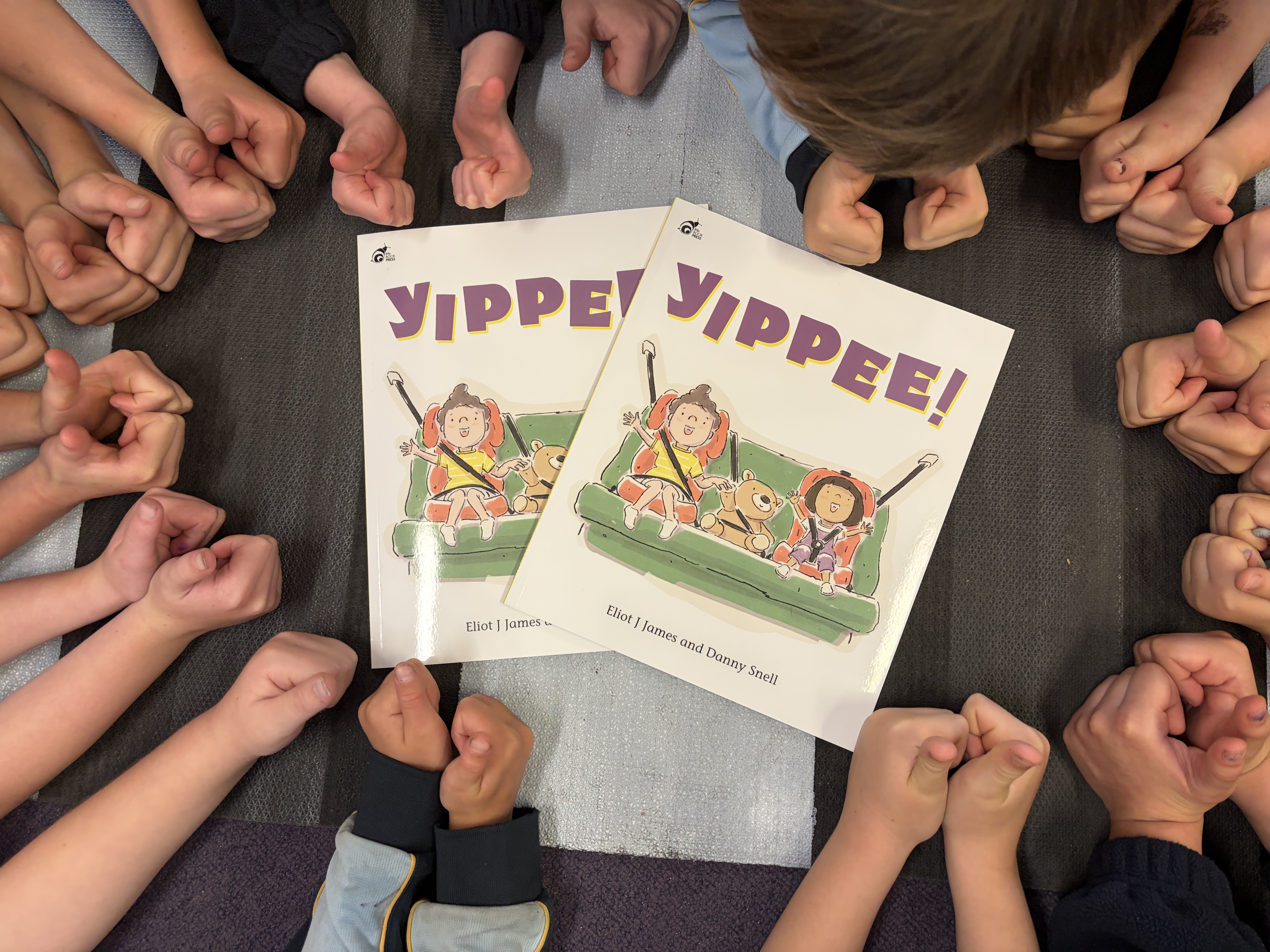 A circle of kids lean over the RACT YIPPEE! picture book, with their thumbs up
