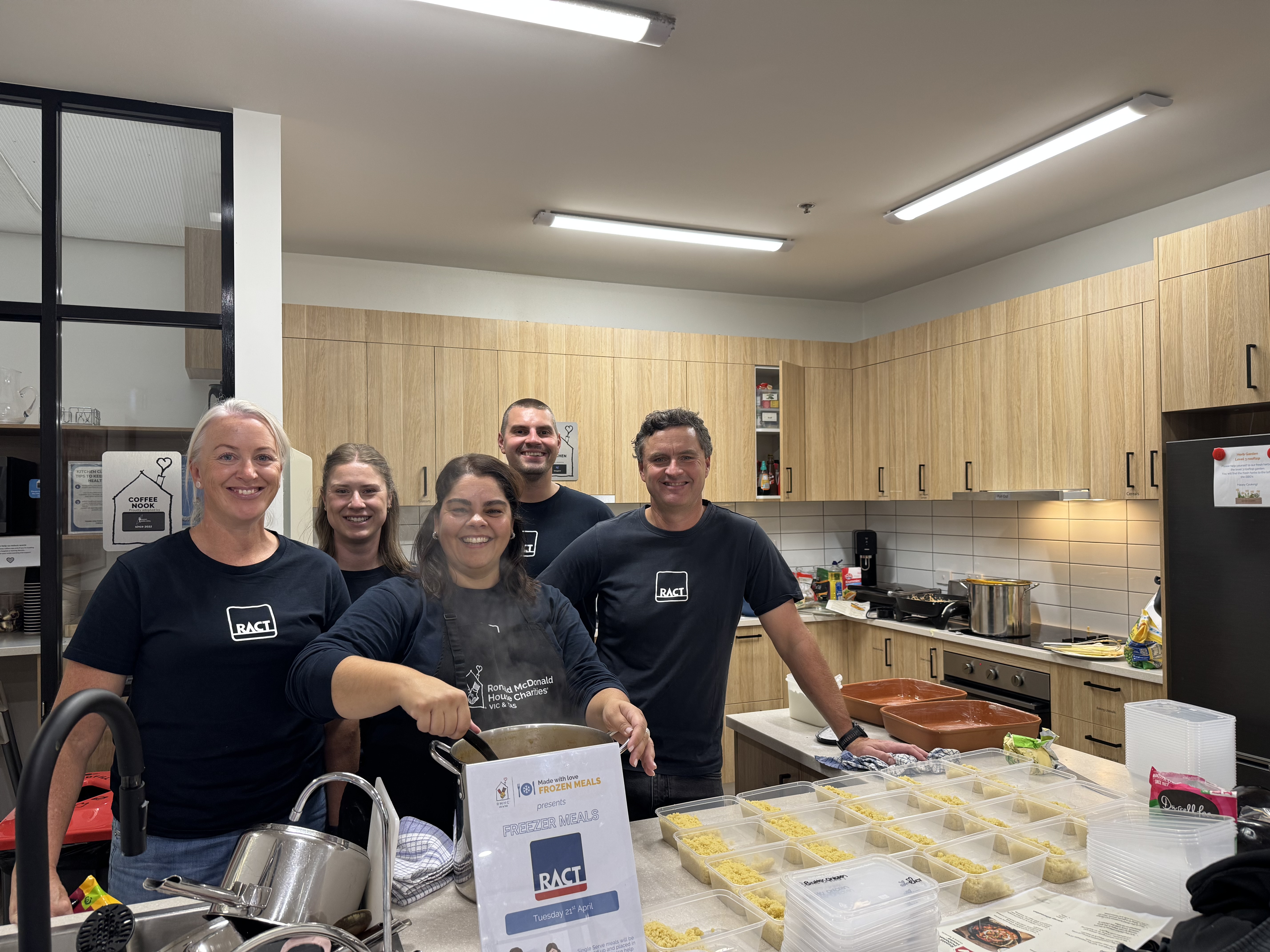 Five smiling people in RACT t shirts package up meals in a kitchen