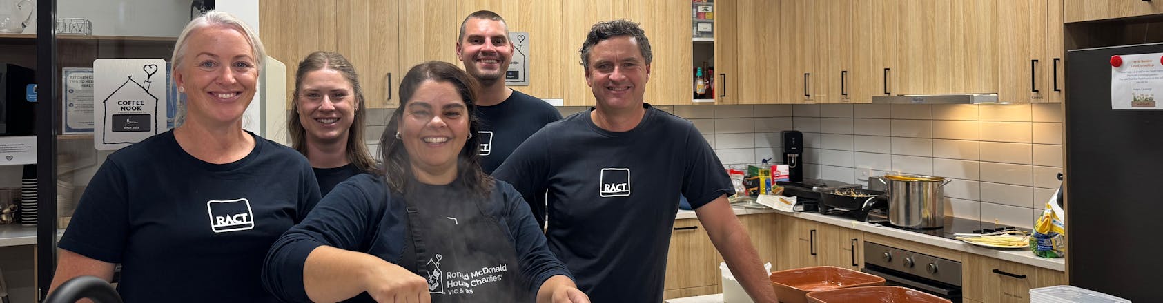 RACT staff volunteering at Ronald McDonald House Five smiling people in RACT t shirts package up meals in a kitchen