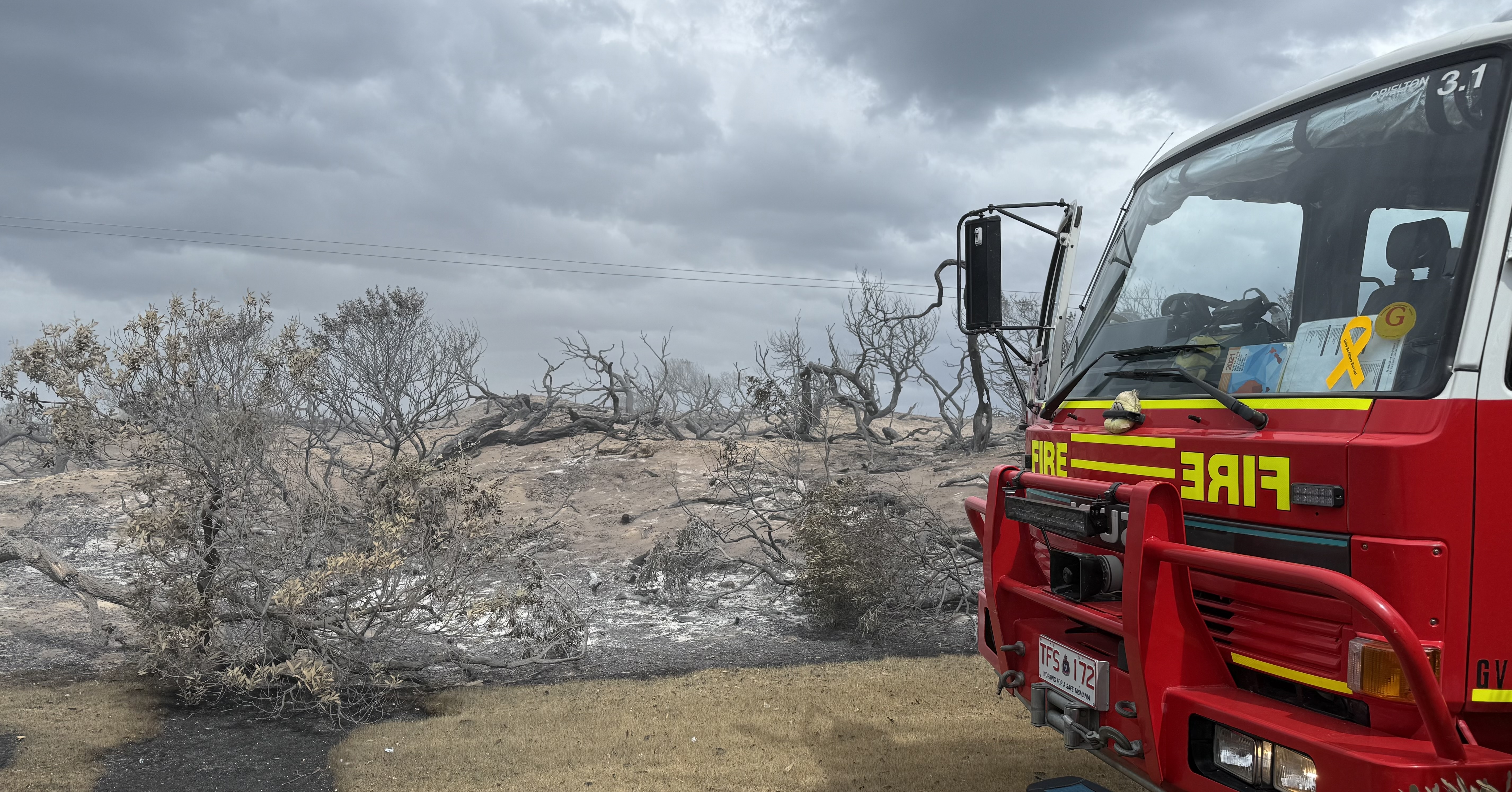 A red fire truck is parked on a gravel road by burnt bush