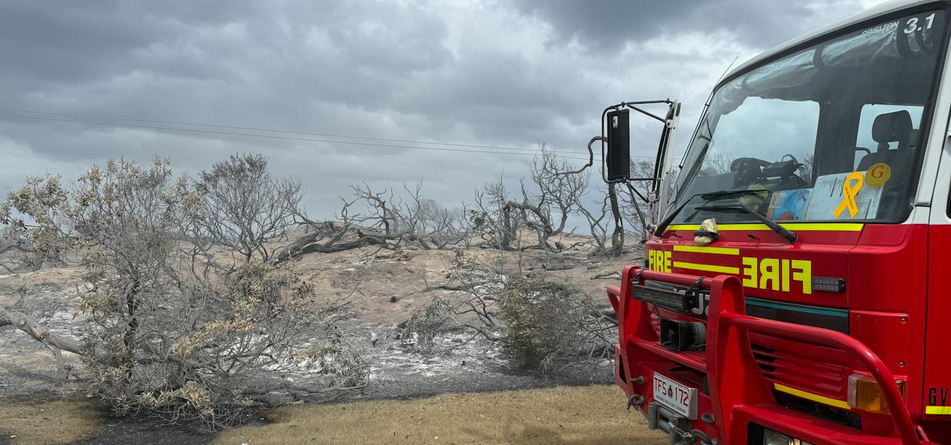 Tasmania Fire Service at the 2025 Dolphin Sands fire. A red fire truck is parked on a gravel road by burnt bush