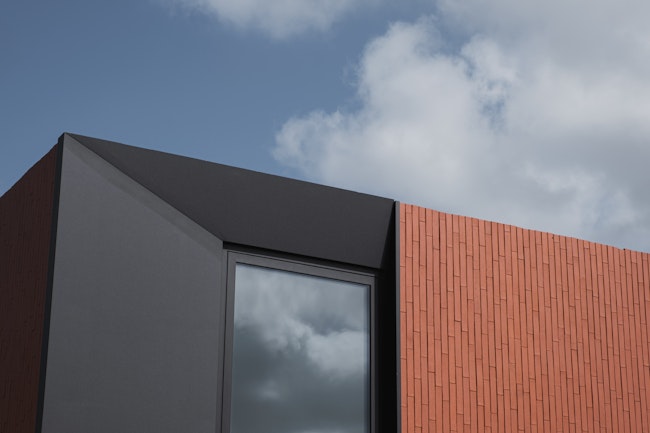 Skilpod modern design houtskeletbouw woning, detail afgeschuind zwart raam en rode steen