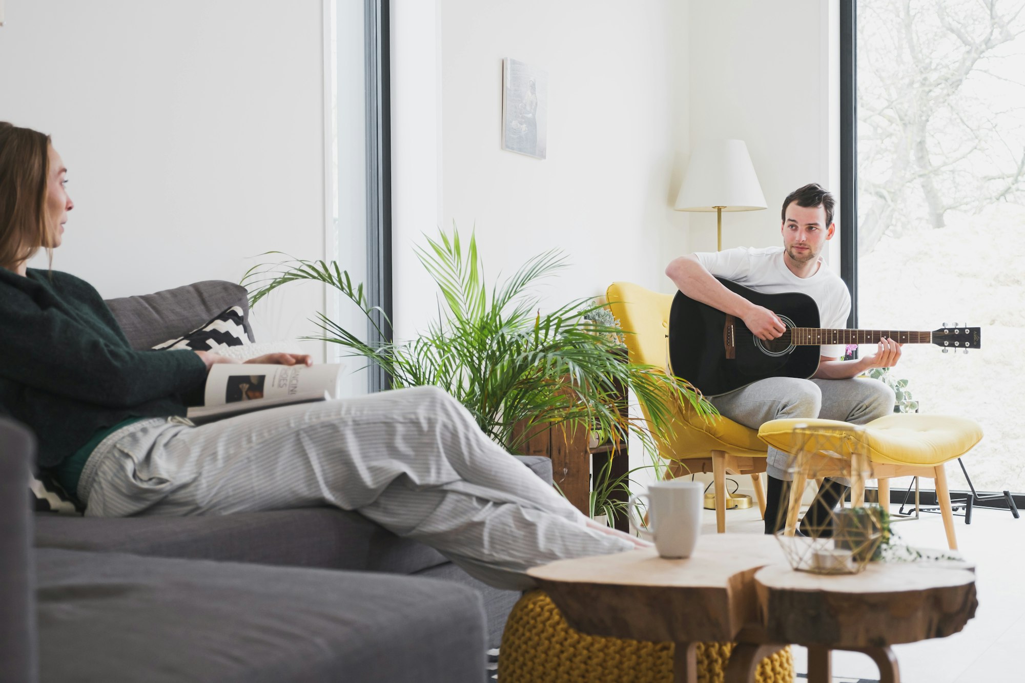 Jonge vrouw kijkt toe hoe jonge man gitaar speelt in de living van een Skilpod