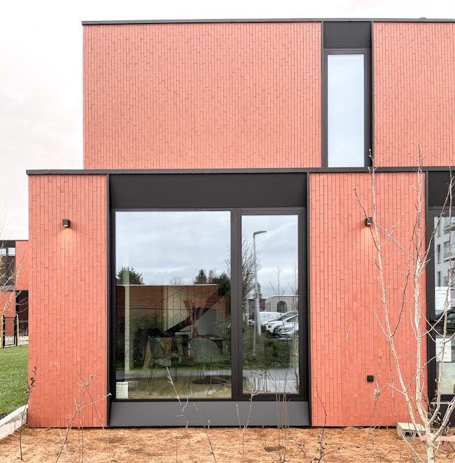 Detail van een #130 Skilpod houtskeletbouw prefab woning met afwerking in rode steen, groot zwart raam