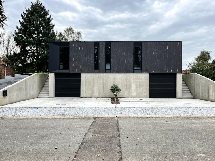 Twee half-open prefab woningen van Skilpod met onderkeldering. Afwerking in zwarte steen.