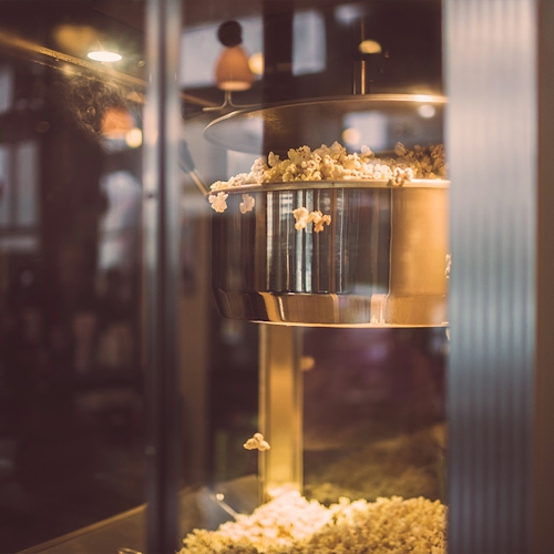 An artistic shot of a class popcorn maker, its metal surface shining almost golden as fresh popcorn cascades out of it. 